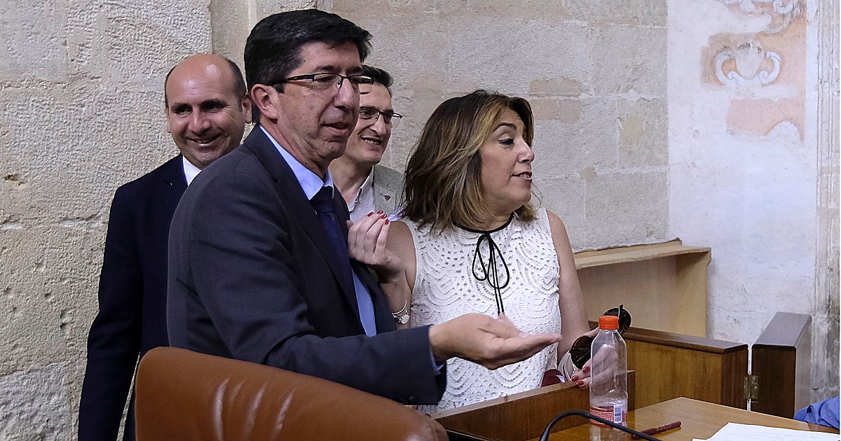 Juan Marín speaking at a political event, with a blurred image of María Jesús Montero in the background.