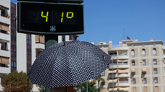 Una persona se protege del sol con un paraguas mientras camina junto a un termómetro que marca 41 grados en Córdoba