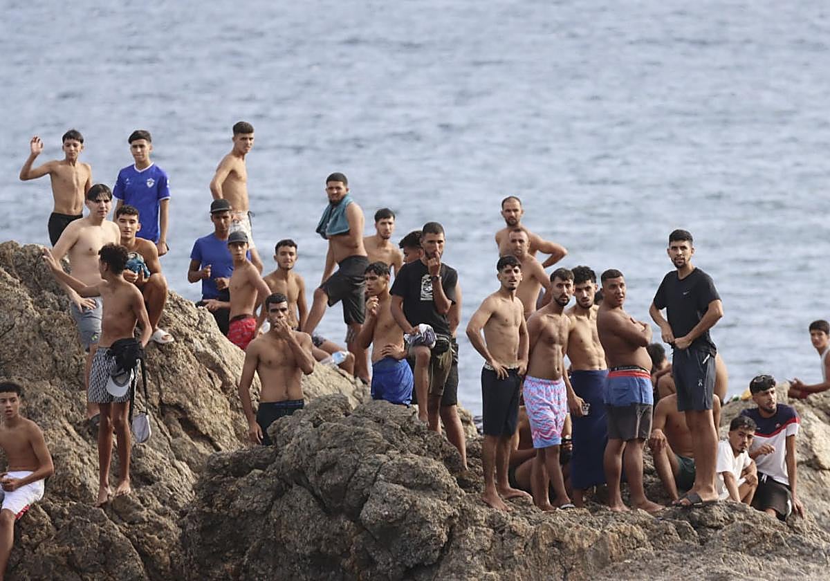 Migrantes observan desde una roca de la playa 'Juan XXXIII' de Ceuta.