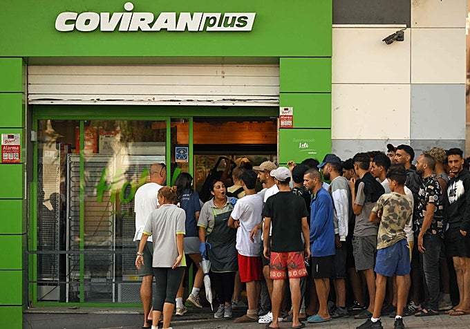 Grupo de inmigrantes agolpados a las puertas de un supermercado.