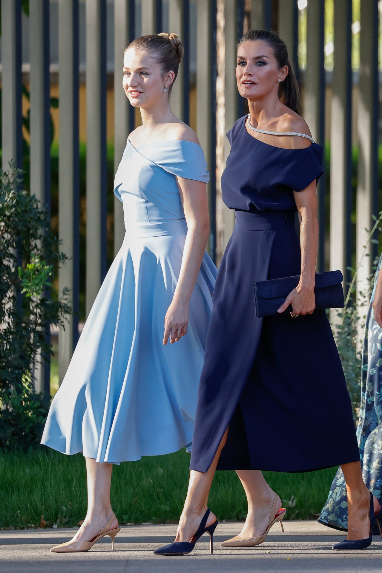 Madre e hija. Doña Letizia y Leonor en absoluta sintonía de estilo: vestidos de largo medio, azules ambos y los dos con escote similar, que dejaba hombros a la vista. El de la madre, en un tono más oscuro, el de la hija en un jovial color cielo. La primera, con un hombro al descubierto y detalle de brillos; la segunda, con escote cruzado sobre el pecho, estilo barco. Ambas, con el pelo recogido y con zapatos tipo salón destalonados.