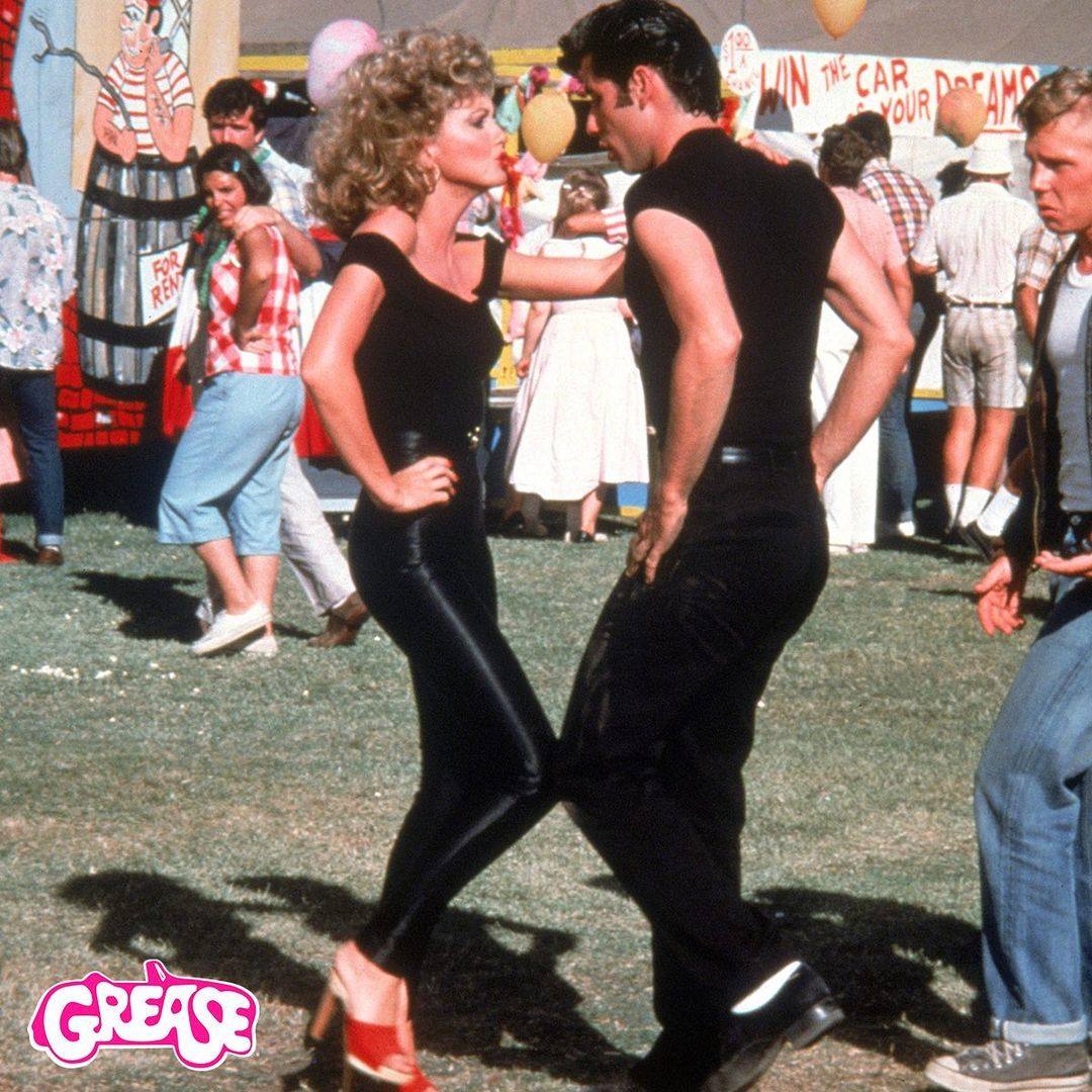 Su look más icónico tiene que ver con uno de los estilismos de Grease, en el que la protagonista lucía un sencillo 'total black' reconocido a lo largo de la historia. El top dejaba los hombros al descubierto y vestía unos leggings de efecto piel ajustados. El pelo ultra rizado y unas sandalias rojas de tacón, y un estilismo, en definitiva muy sexy. Además incluía una chaqueta de tipo 'biker' que ha servido de inspiración en todos los tiempos.