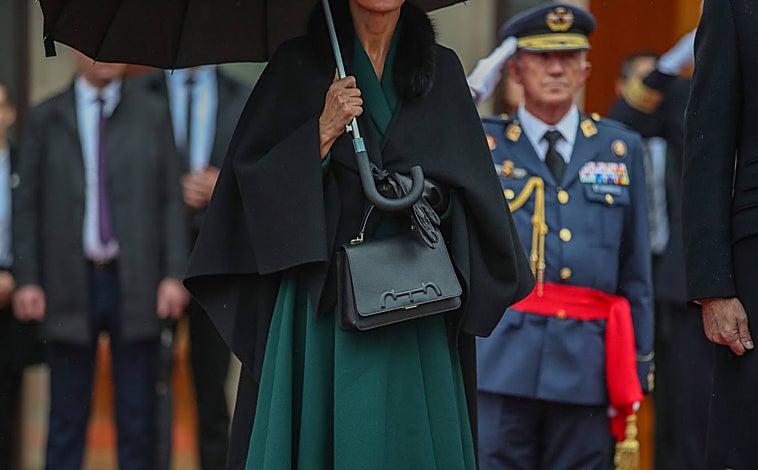 Imagen principal - La Reina ha elegido un vestido abrigo que ya estrenó en color verde botella, con complementos en negro. 