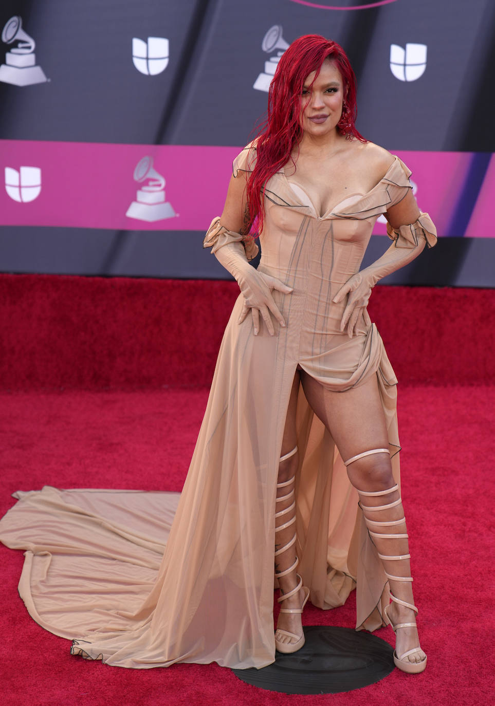 Karol G llevó un peculiar diseño en tonos arena de White Projet en la alfombra roja de los premios Grammy Latinos 2022. Como muchas de las invitadas, la cantante colombiana optó por un vestido escotado y con aberturas en la falda que dejaban al descubierto unas sandalias con tiras que llegaban por encima de la rodilla. Además lo combinó con guantes del mismo tono.
