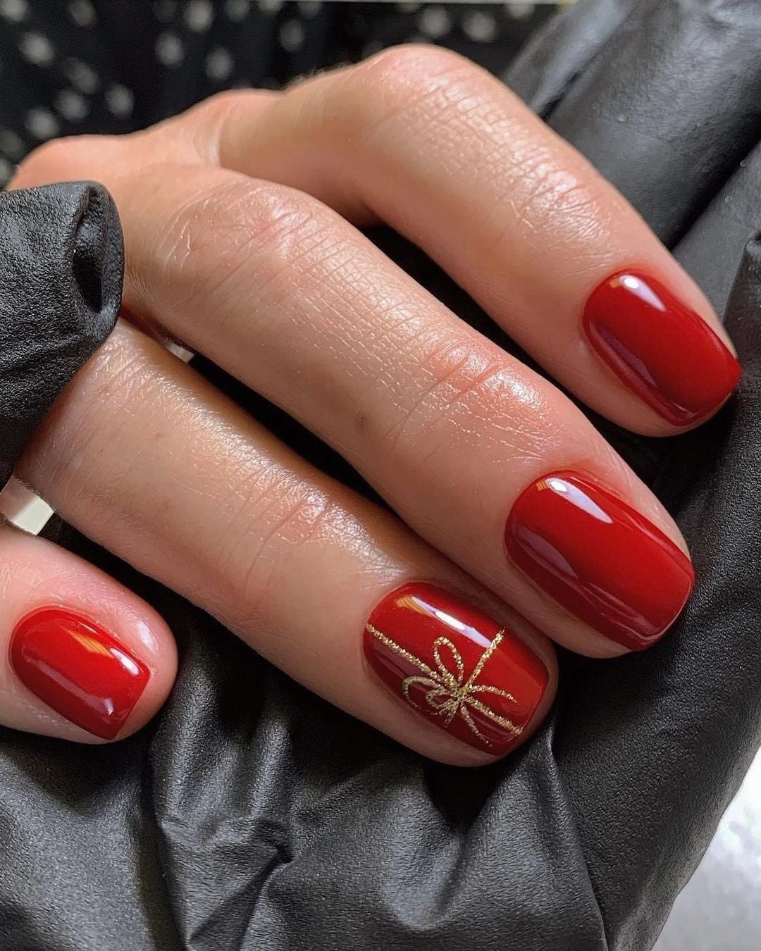 Manicura roja con un detalle dorado del típico lazo de regalo. Una manicura discreta, elegante y muy apropiada para la navidad. 