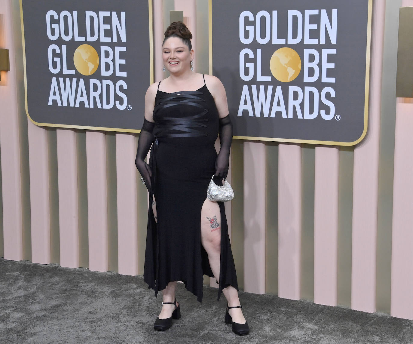 Megan Statler con un vestido negro de tirantes, con la parte superior de tiras, abertura en una pierna y guantes transparentes. 