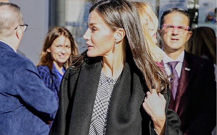 Imagen principal - La reina con un estilismo muy elegante formado por abrigo negro, vestido con estampado Príncipe de Gales, y botas altas de ante. 