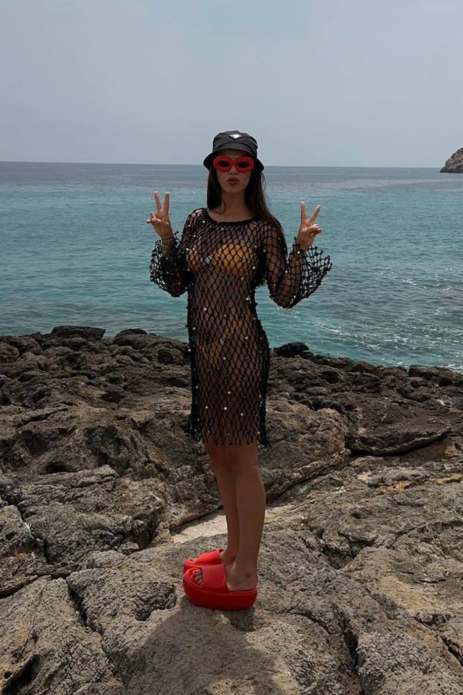 Violeta combinó un bikini amarillo con un vestido negro de rejilla, un gorro pescador de Prada y unas sandalias y gafas de sol rojas. 