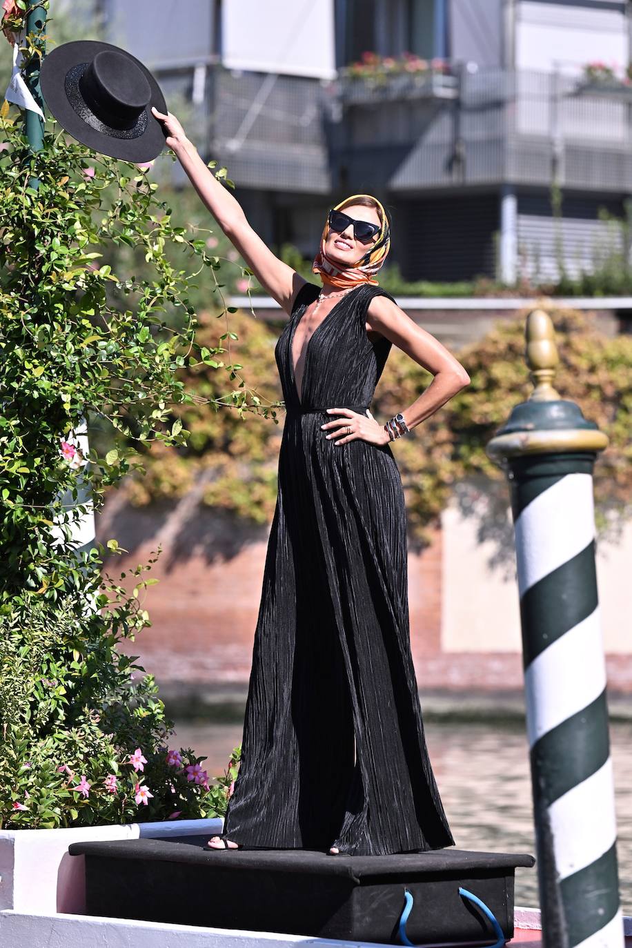 Nieves Álvarez llegó a Venecia más espectacular que nunca. Lució un mono negro plisado de satén, de escote en pico y con un cinturón de Atelier Pronovias. Como complementos, al más puro estilo veneciano, apostó por un pañuelo colorido en el pelo, un sombrero y unas gafas de sol.  