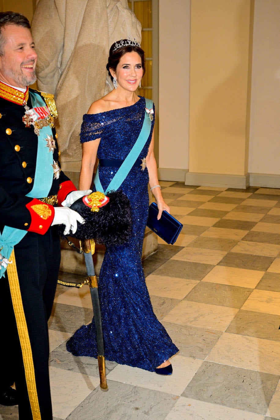 La madre del homenajeado, la princesa Mary de Dinamarca, eligió un vestido de escote asimétrico en color azul noche con lentejuelas, que combinó con clutch de Prada y zapatos en el mismo tono de Gianvito Rossi. Lució también tiara y pendientes largos de diamantes. 