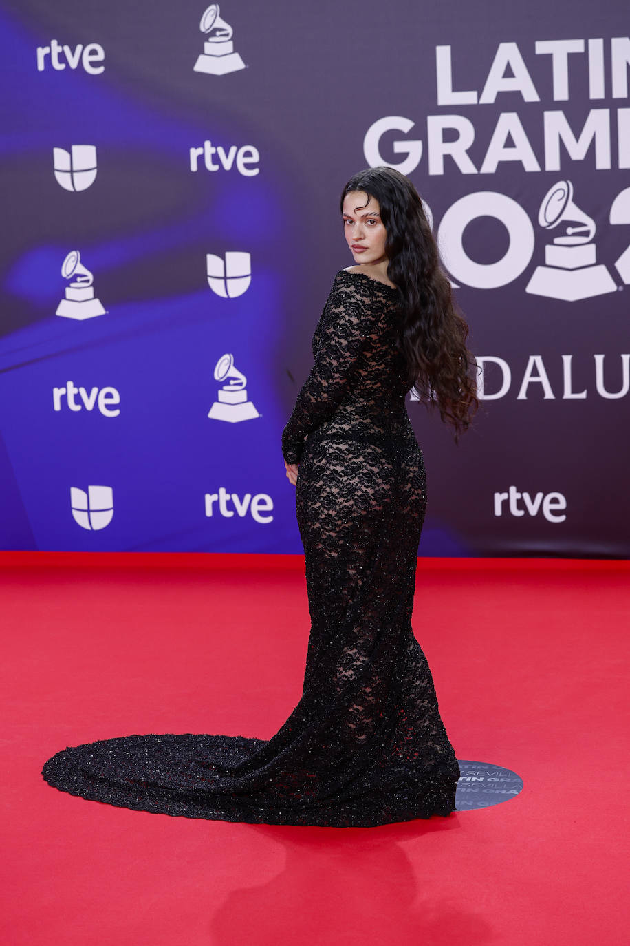 Rosalía con vestido negro largo con cola de encaje y melena suelta con rizos en los Premios Grammy Latinos 2023. Es un modelo de la colección primavera-verano 2024 de Balenciaga. 