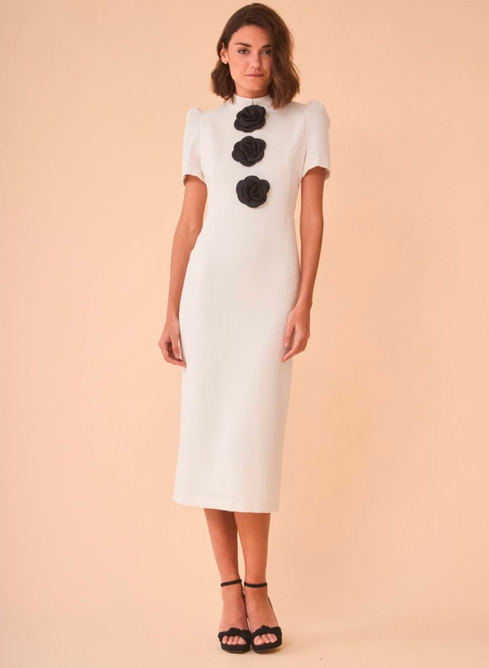 Vestido de tweed en blanco con cuello subido y manga corta, decorado en el pecho con tres flores negras. 160 euros en Coosy.