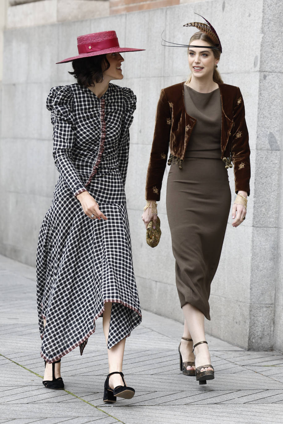 Invitadas con originales vestidos. por un lado en color marrón con chaqueta de terciopelo y tocado de plumas; y por otro con estampado 'vichy', estructura asimétrica y sombrero de rafia en color fucsia. 