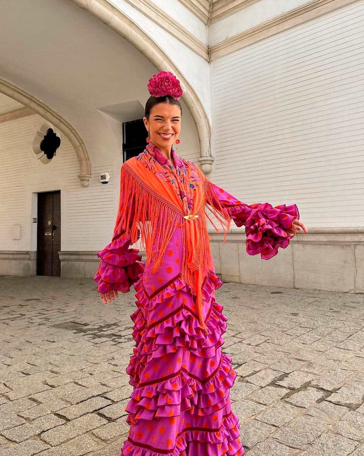 La 'influencer' sevillana Elena Gortari llevó el domingo de feria un vestido morado con lunares en contraste naranjas. El mantón, también naranja con toques florales lila y la flor en el pelo, a juego con el vestido. 