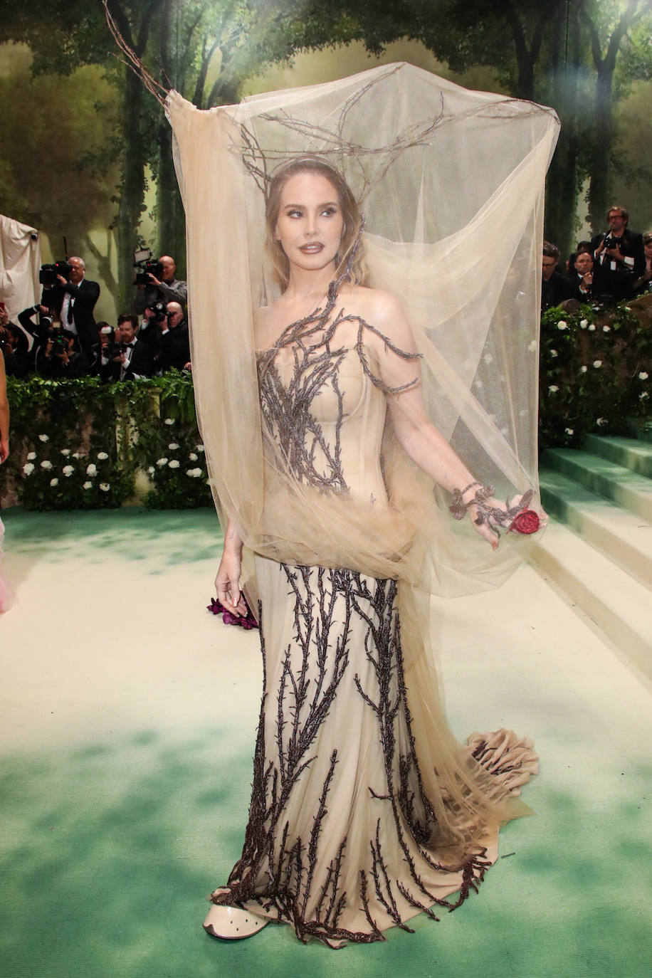 Lana del Rey lució uno de los estilismos más arriesgados con un diseño en tono nude que emulaba la rama de un árbol.  La cantante lució además maquillaje de Charlotte Tilbury en tonos nude y labios perfilados. 