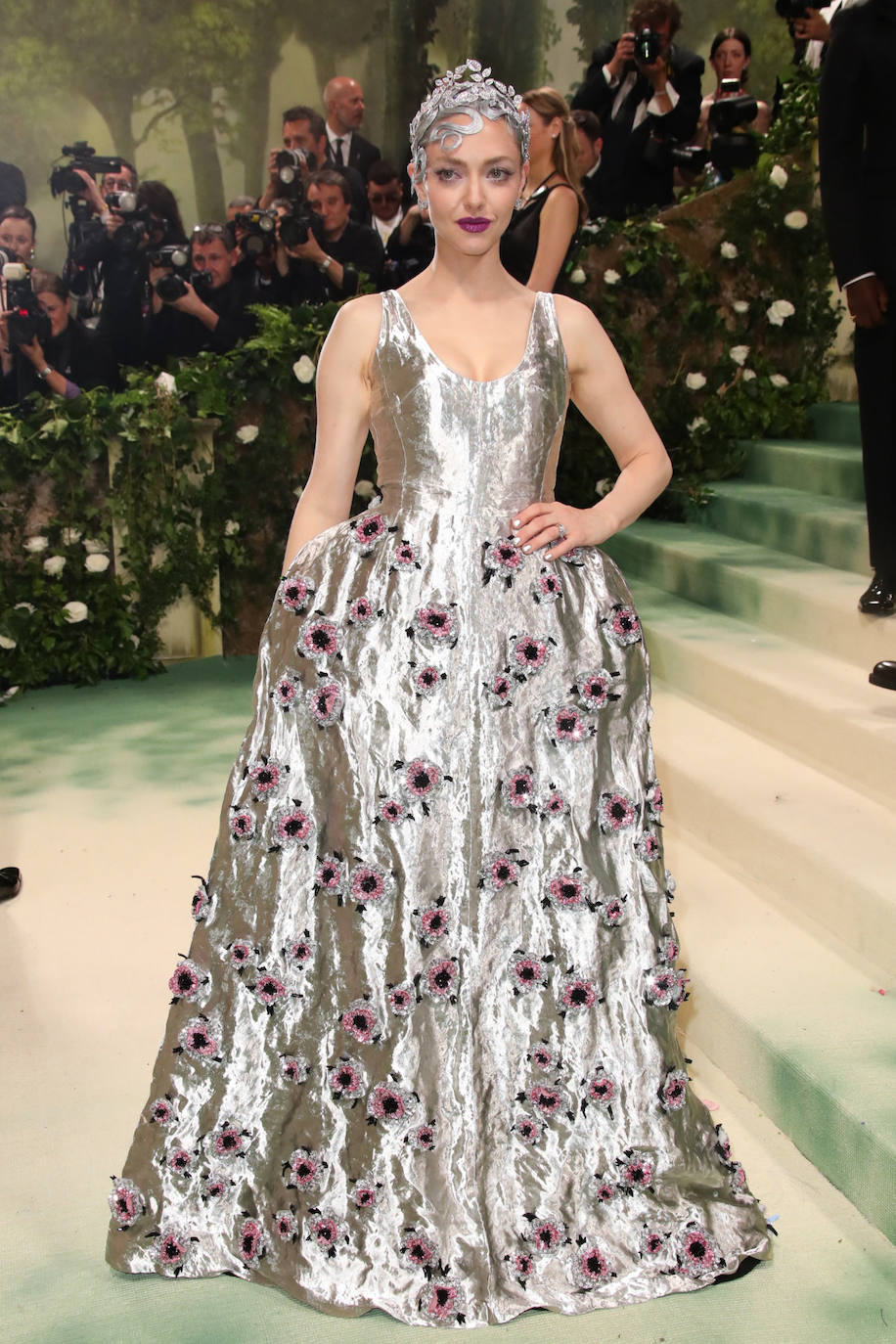 Amanda Seyfried eligió un vestido metalizado con detalles de flores, de Prada, y un tocado plateado que cubría toda su melena, de Chaumet. También llevó de la misma firma los pendientes Joséphine Duo Eternel, y los anillos Laurier y Joséphine Aigrette Impériale. En su maquillaje, resaltaron sus labios en fucsia, a juego con las flores de la falda. 