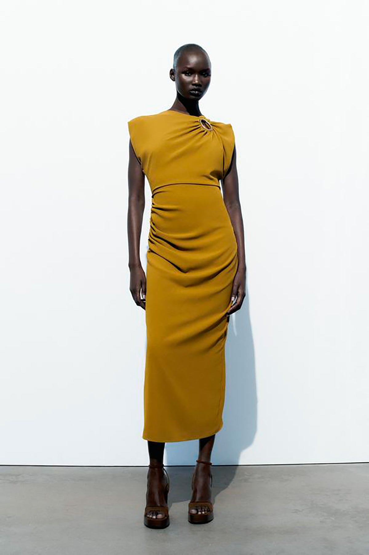 Vestido midi de cuello redondo con aplique dorado, manga a la sisa y detalle de frunces. 39.95 euros en Zara. 