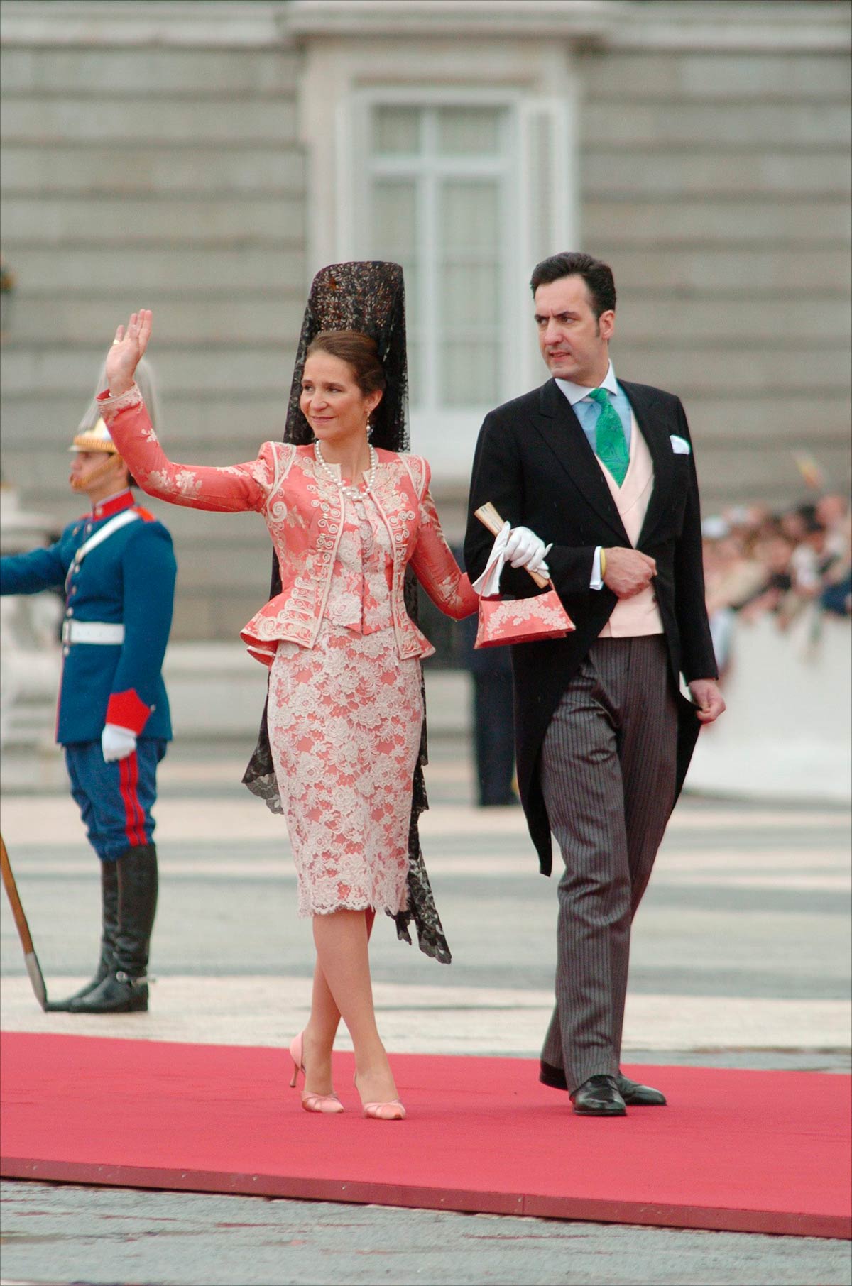 La Infanta Elena, también con una mantilla negra como Doña Sofía, lució un look compuesto por un vestido midi en rosa con bordados blancos y una chaqueta a juego firmado por Christian Lacroix Alta Costura. Lo combinó con unos guantes, un bolso de mano y un collar y pendientes de perlas.  