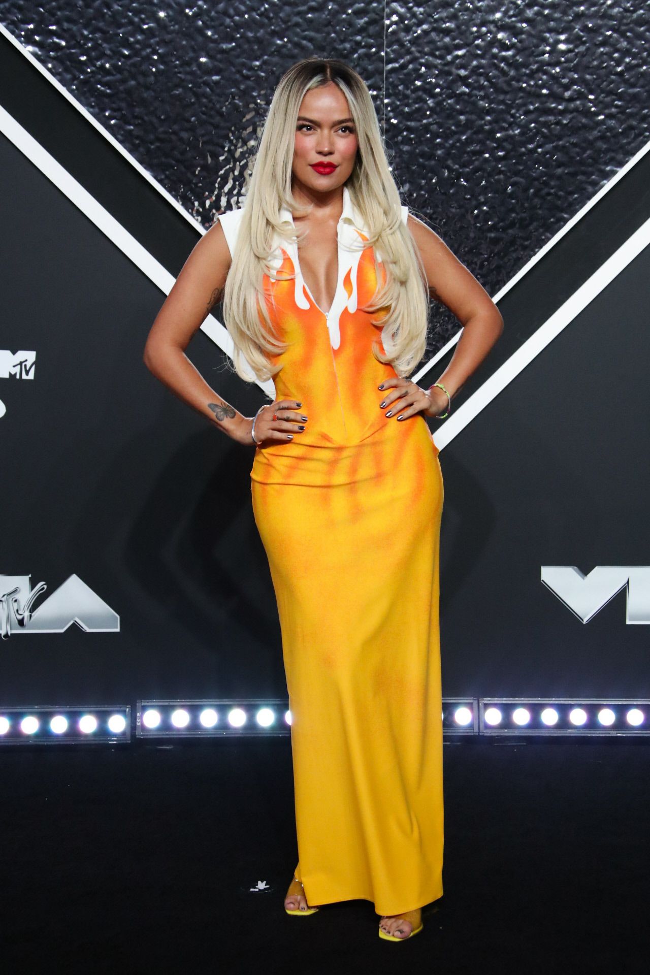 Karol G llevó el color a la alfombra roja de los MTV con un vestido en tono amarillo, que imitaba una llama de fuego. Es un modelo vintage de Véronique Leroy. Lo combinó con su melena suelta, peinada con raya en el medio y labios rojos. 