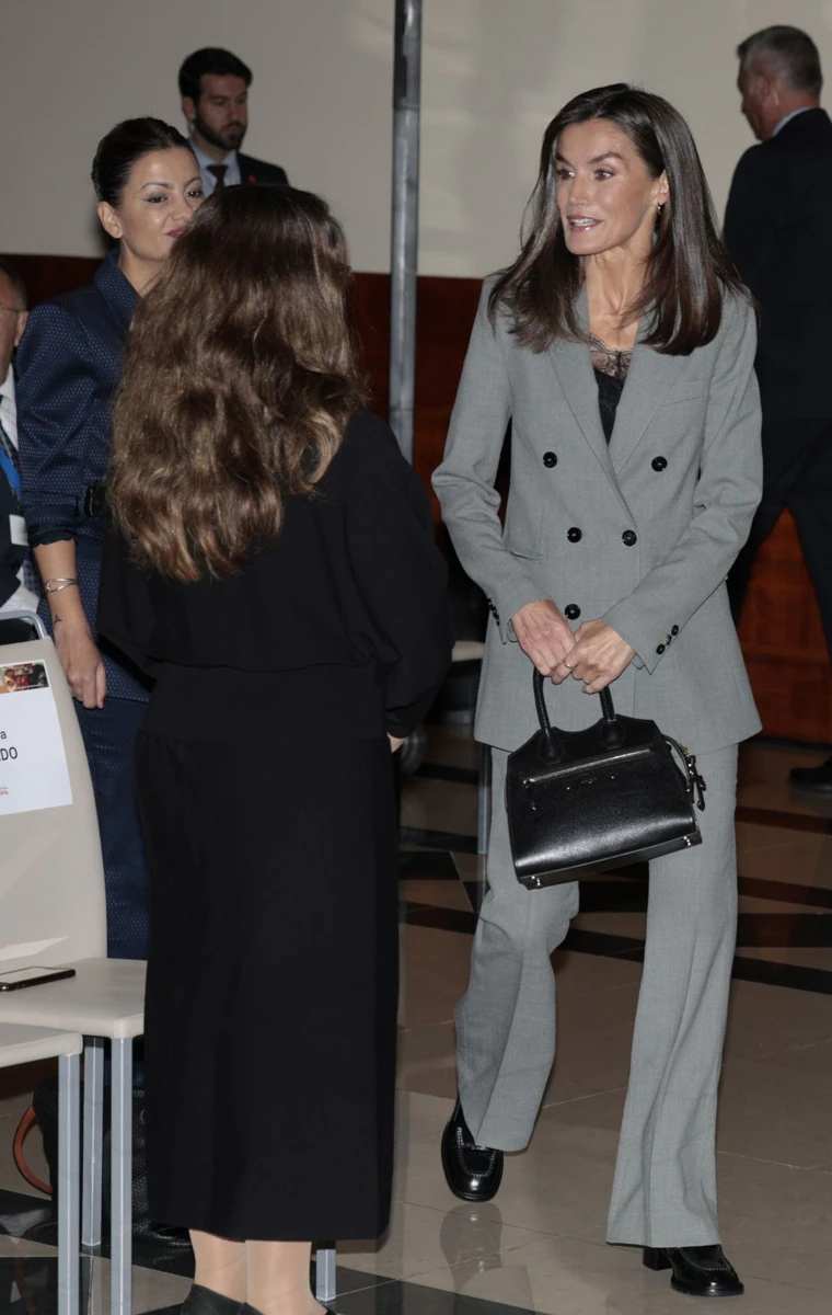 La Reina con traje gris, top lencereo y mocasines.