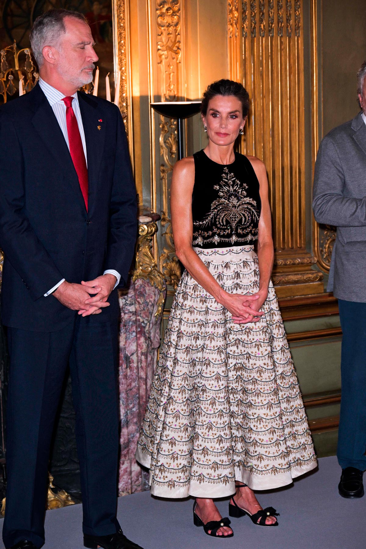 La Reina Letizia en la ceremonia de recepción del Equipo Olímpico Español en París. La soberana, junto a su marido Felipe VI, aterrizó en la capital de Francia con motivo de los Juegos Olímpicos y escogió uno de sus mejores looks hasta la fecha, un diseño de Alta Costura de Dior con el que hizo un guiño al país vecino. Estaba formado por una voluminosa falda beige de seda con aplicaciones doradas y un cuerpo negro de terciopelo también con detalles en dorado. En los pies, unas sandalias de tacón bajo con un lazo. 