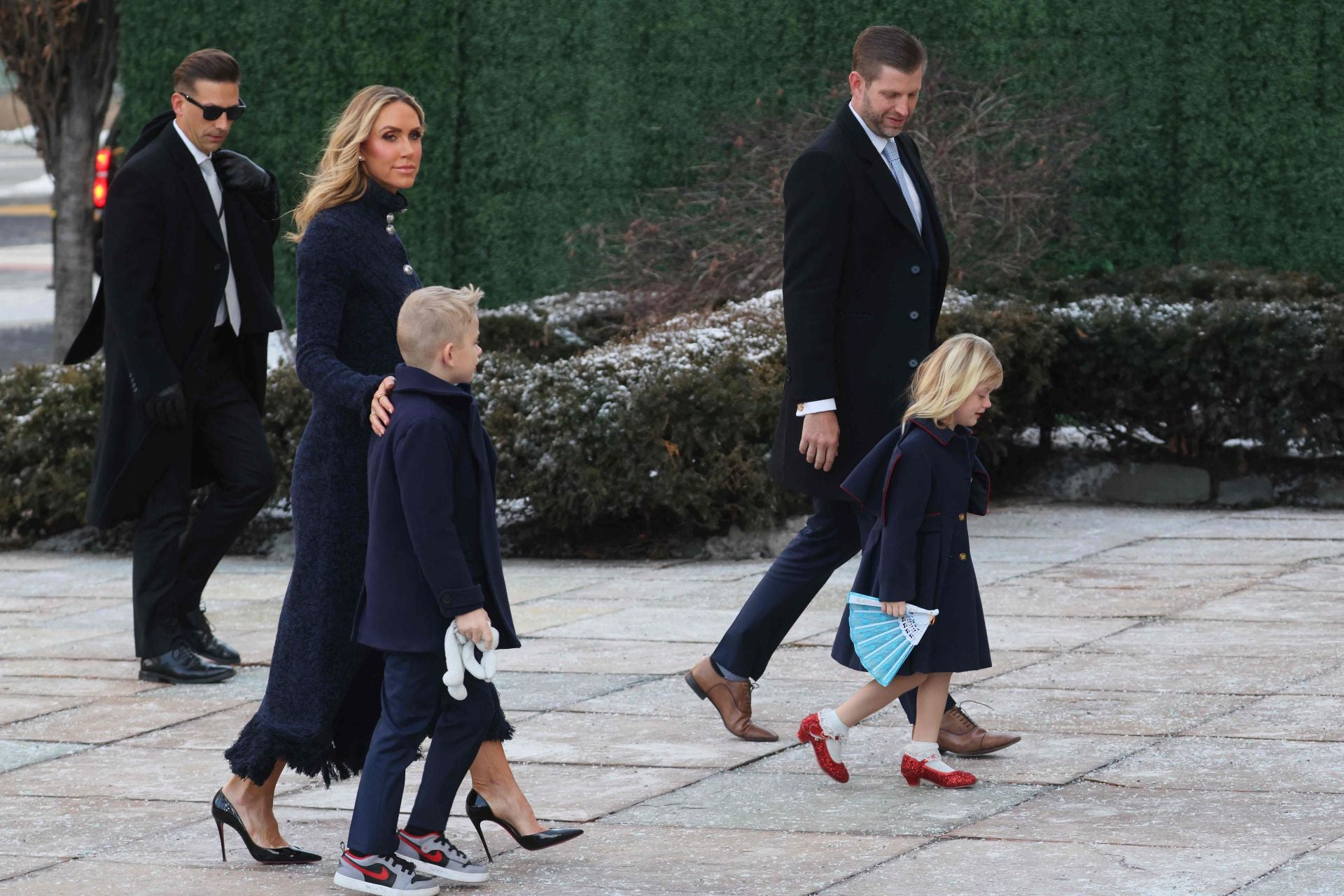 Lara Trump con abrigo azul con tejido brocado, botones plateados y bajo con flecos, junto a Eric Trump y sus hijos.