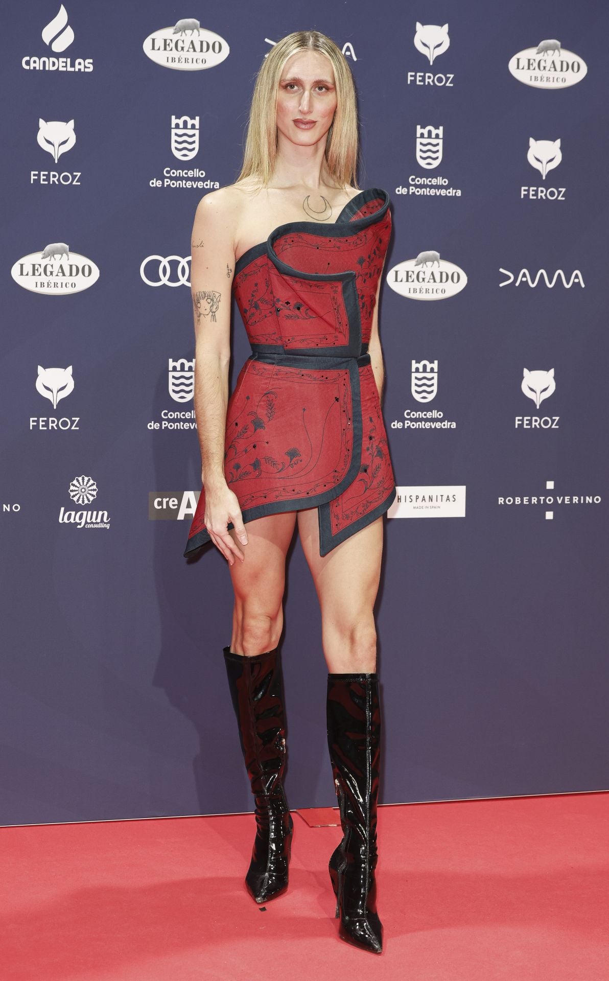 Álex de la Croix con look asimétrico de Álvaro Calafat en color teja con ribete azul combinado con botas altas en color negro. 