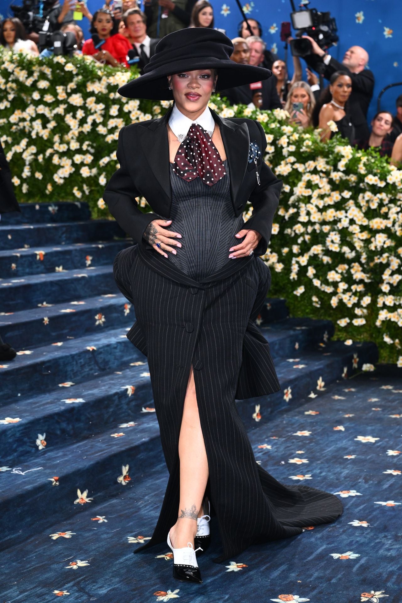 Con 'total look' firmado por Marc Jacobs compuesto por una chaqueta torera, una falda larga voluminosa con estampado de rayas diplomáticas y una corbata de satén con lunares, Rihanna ha presumido de embarazo sobre la alfombra de la gala Met.