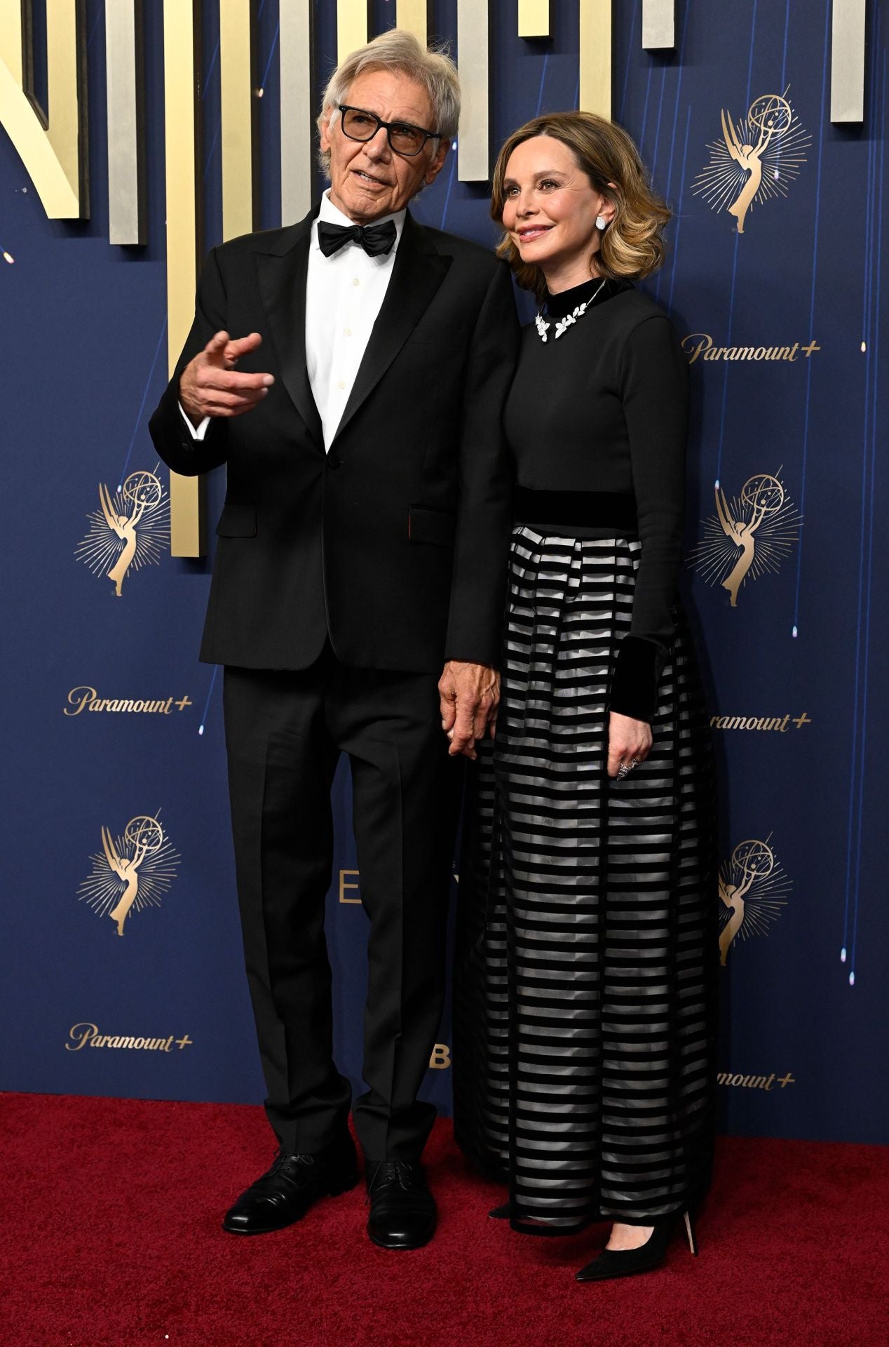 Harrison Ford con clásico esmoquin negro y Calista Flockhar con conjunto de falda y top de manga larga. 