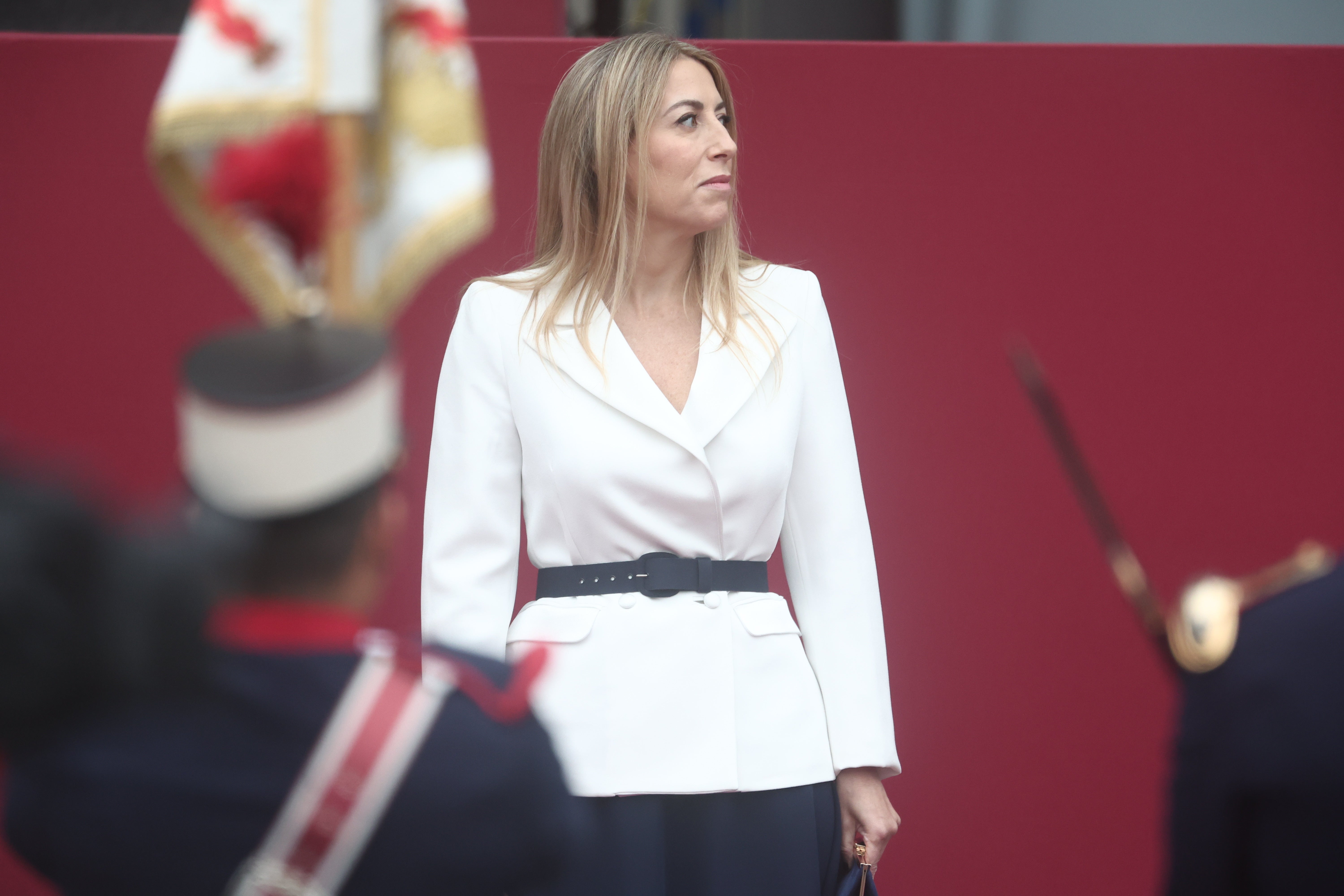 La presidenta de Extremadura ha sido alguna de las invitadas que ha apostado por una opción distinta al vestido, en su caso con blazer blanca cruzada de doble botonadura que ciñe la cintura gracias a un cinturón azul marino a tono con la falda midi de vuelo de su estilismo. 