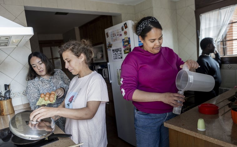 Imagen principal - Arriba, las madres, en la cocina, supervisadas por la educadora social. Abajo a la izquierda, Ella, con su bebé, Isabella, y a la derecha, el cartel que adorna la entrada