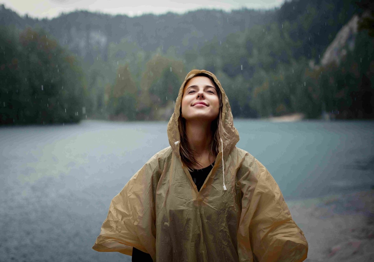 Una mujer disfrutando de la lluvia en el bosque con un chubasquero