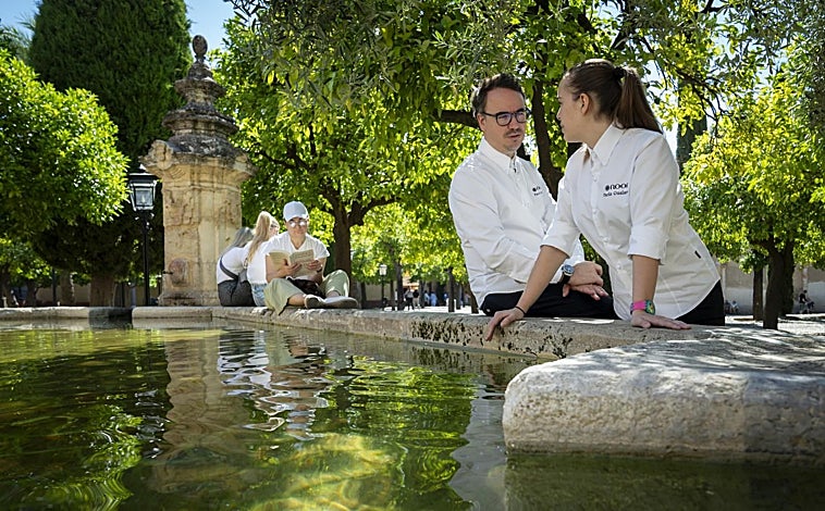 Imagen principal - Paco Morales y Paola Gualandi, en varios puntos de la ciudad de Córdoba. Arriba, en una de las fuentes del patio de los naranjos de la mezquita de Córdoba. Abajo, a la izquierda, en el restaurante El Churrasco que suelen frecuentar en sus días libres. A la derecha, juntos caminando por una de las calles de la judería.