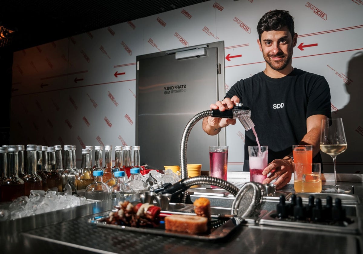 Nico Miranda, bartender de SubCero, la última y más novedosa coctelería de Madrid, sirviendo uno de sus cócteles de tanque con una manguera. En primer plano, los bocados de Sala Cero que los acompañan