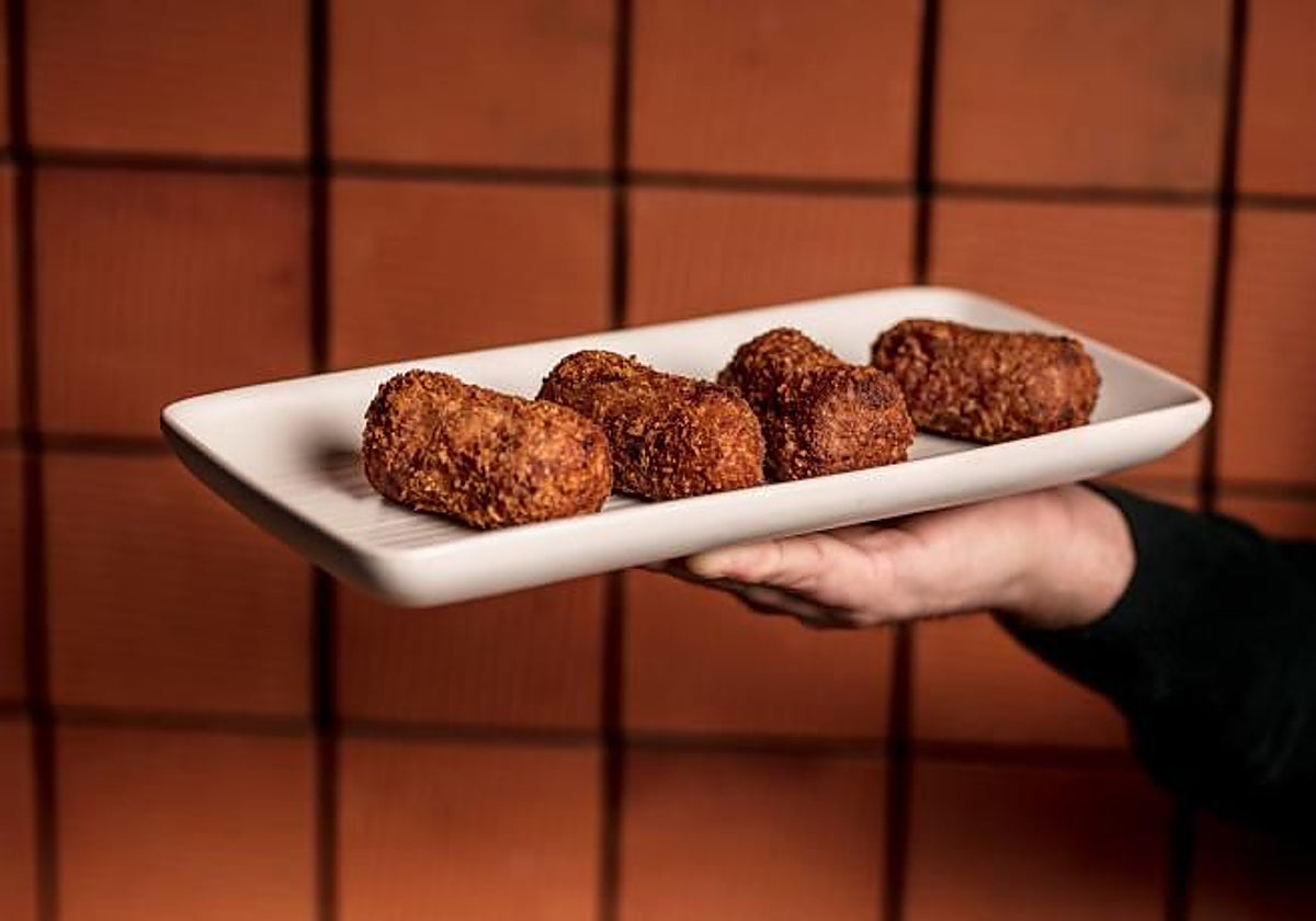 Un camarero portando un plato de croquetas