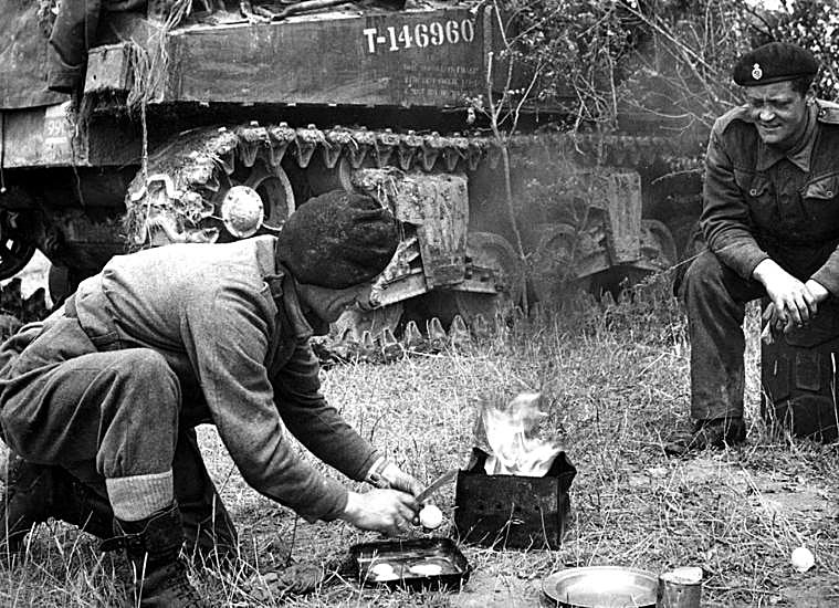 Two tank soldiers preparing food in front of their tank