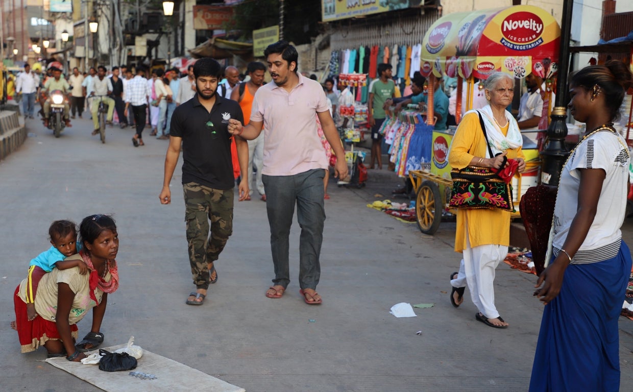 Con las manos y las piernas dobladas por la polio, una joven pide limosna cargando a su bebé sobre la espalda