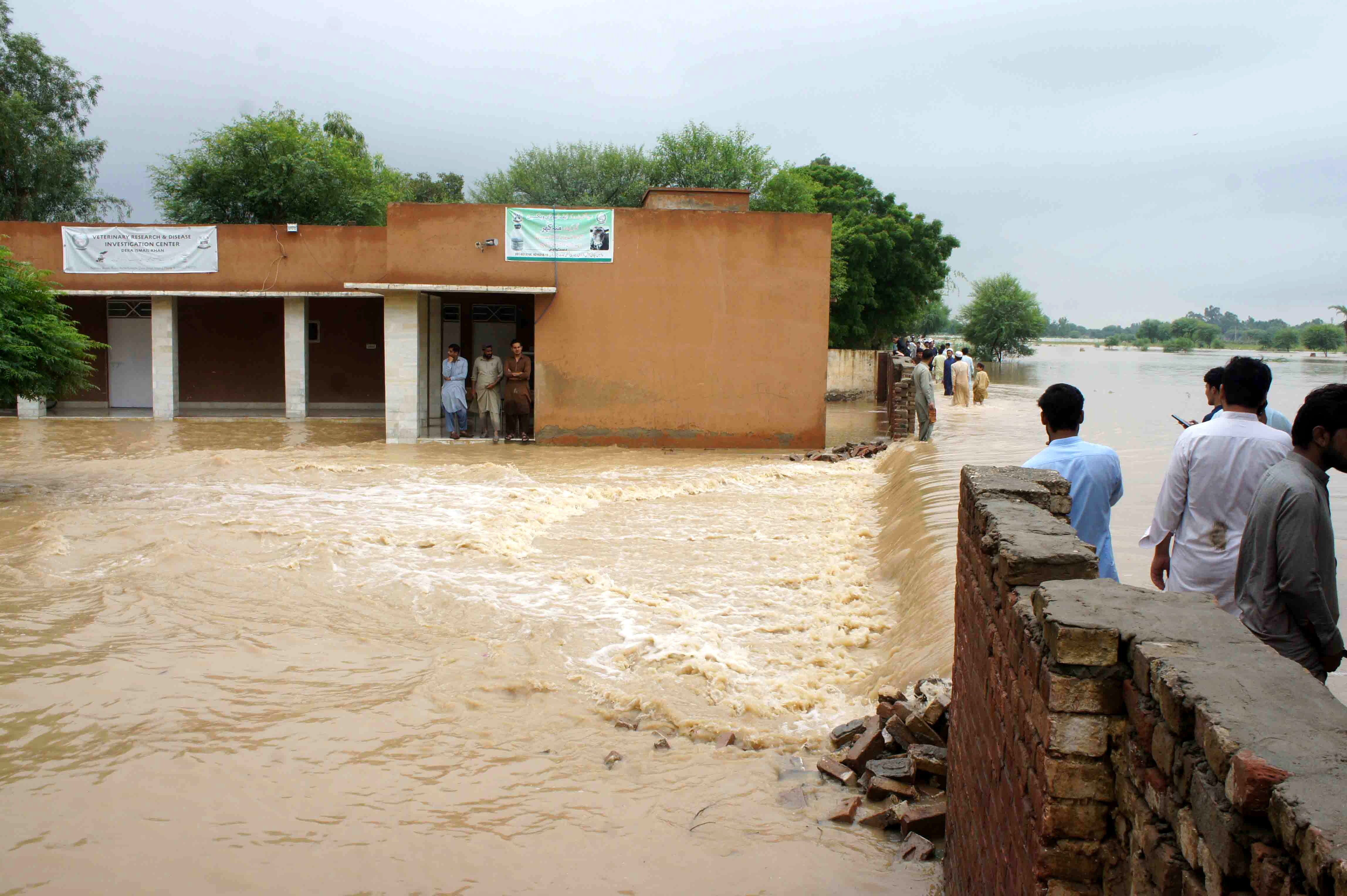 Personas esperan en Dera Ismail Khan para poder pasar a través de un calle inundada.
