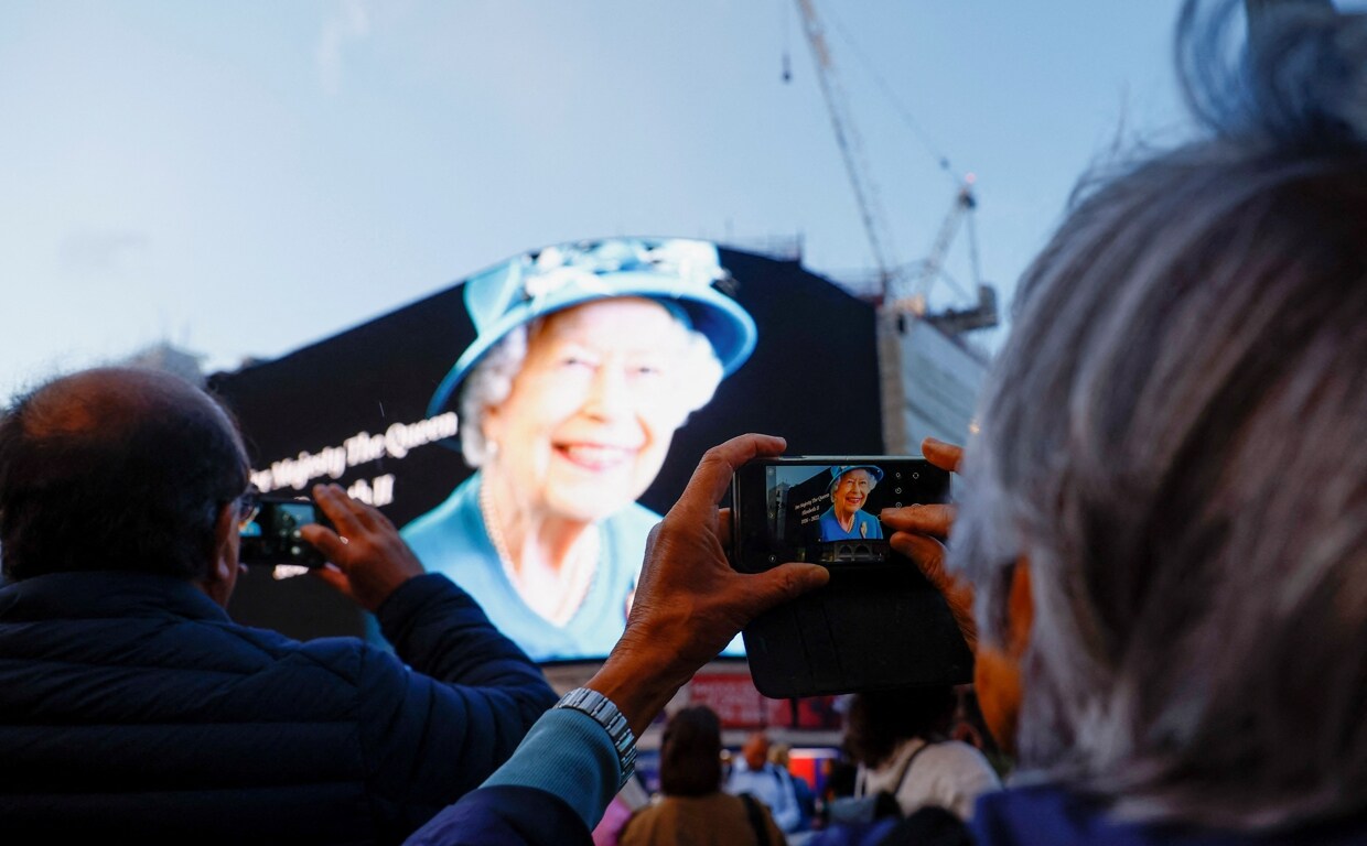 Varias personas toman fotografías de la imagen que anuncia el fallecimiento de la Reina Isabel II, que se proyectaron ayer en una pantalla en Piccadilly Circus, en el centro de Londres