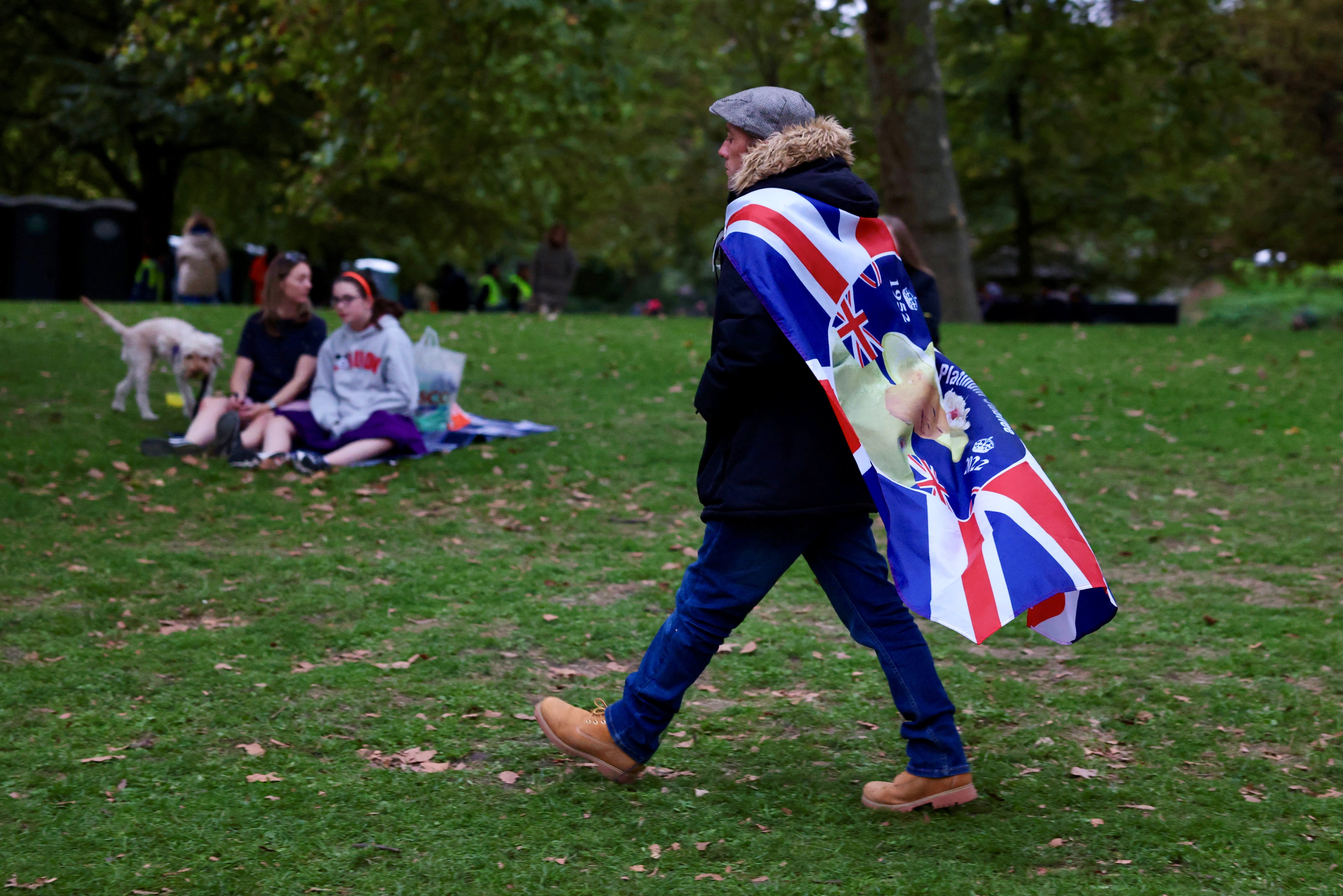Un hombre con una bandera de la Union Jack a la espalda camina por un parque cerca de The Mall, la calle por donde pasará la procesión fúnebre de la Reina Isabel II. 