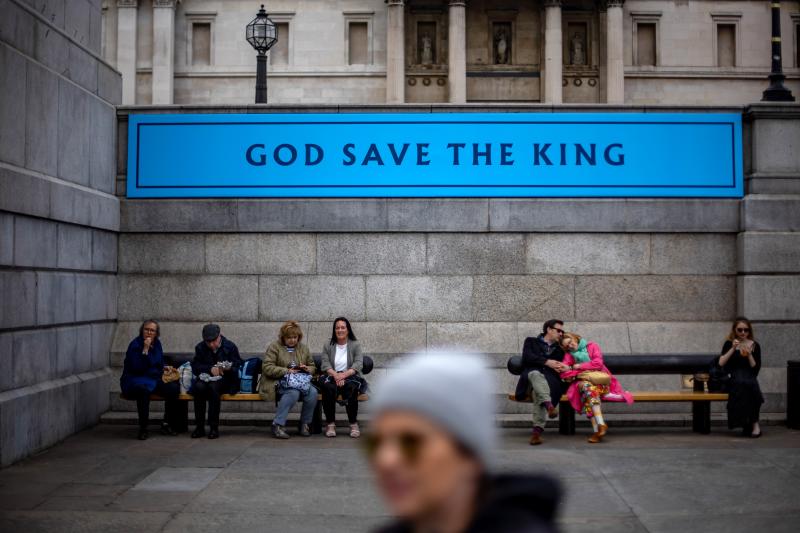 La gente descansa debajo de una pancarta donde puede leerse "Dios salve al Rey"