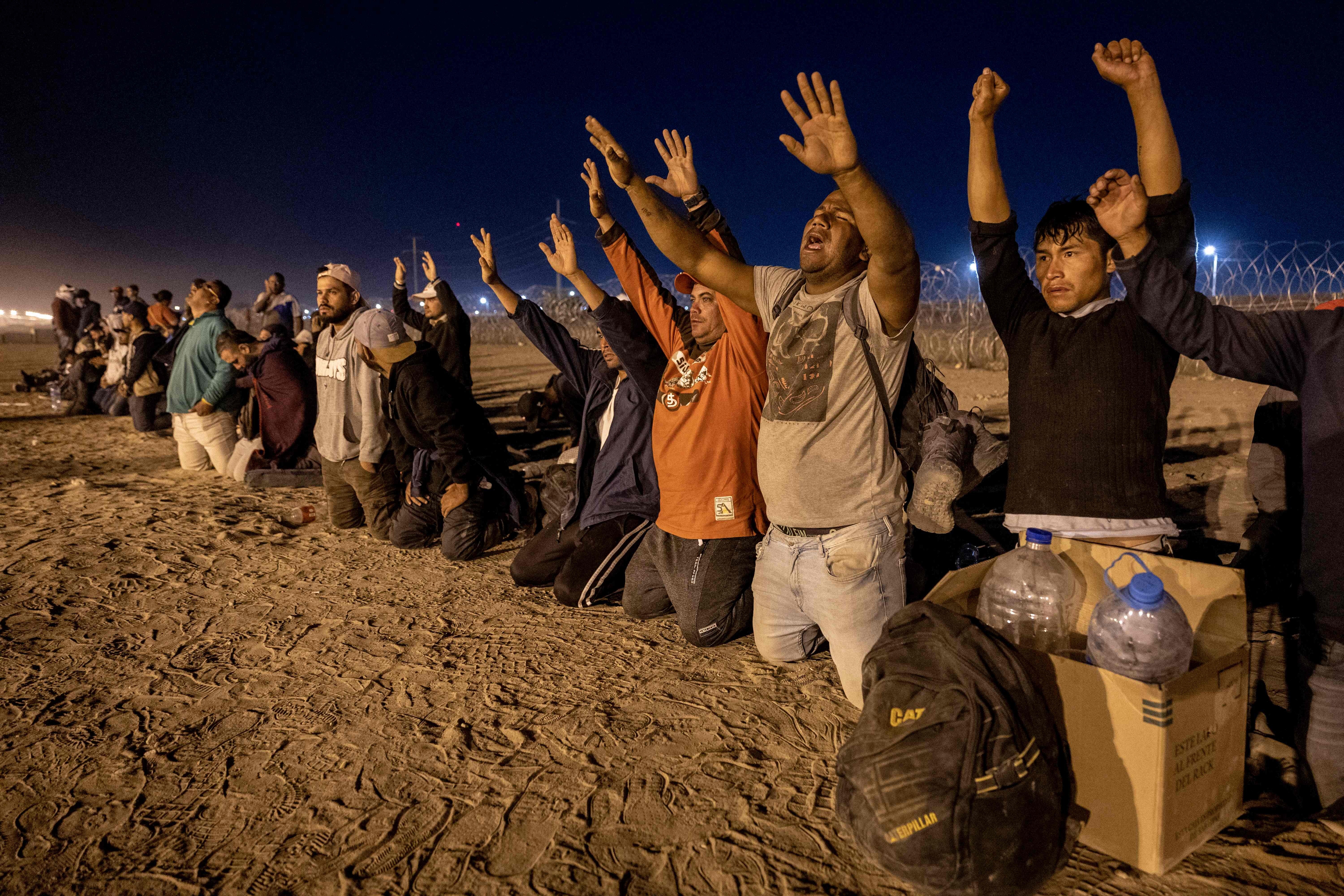 Inmigrantes rezan mientras esperan que los agentes fronterizos estadounidenses les tramiten el asilo tras cruzar desde México