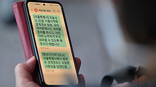 Una mujer muestra su teléfono móvil con un mensaje de texto de advertencia de evacuación de emergencia emitido por la ciudad de Seúl