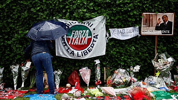 Una persona deja una carta entre flores y recuerdos futbolísticos cerca de Villa San Martino, la residencia del ex primer ministro italiano Silvio Berlusconi, a la que fue trasladado su cuerpo tras su muerte