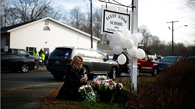 Una mujer deposita flores en un monumento conmemorativo junto a una señal de la escuela primaria Sandy Hook