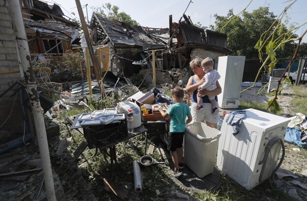 Local residents inspect damage at the site hit by falling debris from a missile in a village near Kiev