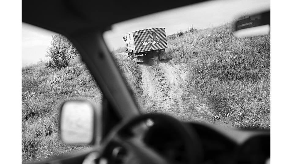 Un convoy de una unidad de desminado de los servicios de emergencia de Ucrania circula por una pista de tierra entre campos minados.
