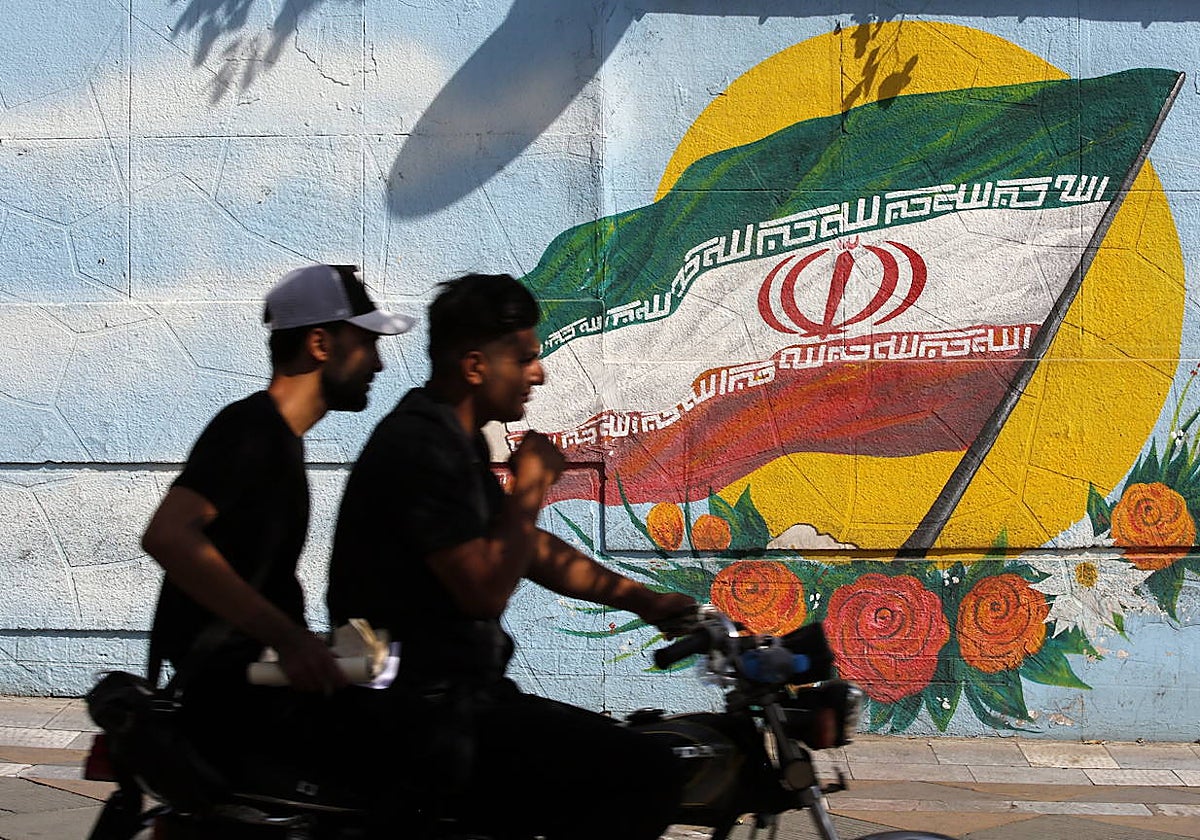 Dos personas pasan junto a un mural de la bandera nacional de Irán en una calle de Teherán