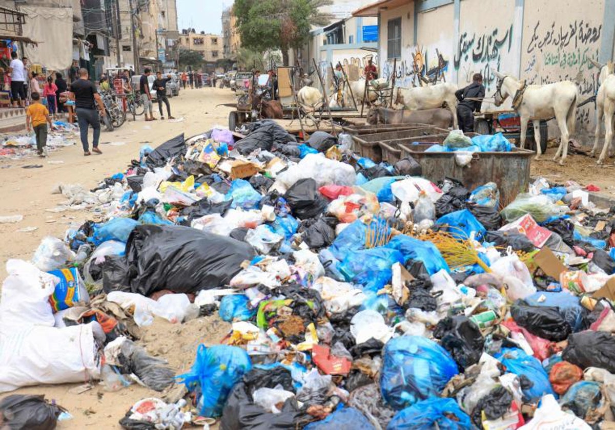 Residentes de la franja de Gaza caminan junto a la basura acumulada en la calle