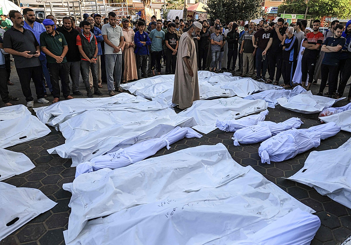 Un hombre camina entre los cuerpos envueltos en sudarios de los muertos en bombardeos israelíes en Deir Balah, en el centro de la franja de Gaza